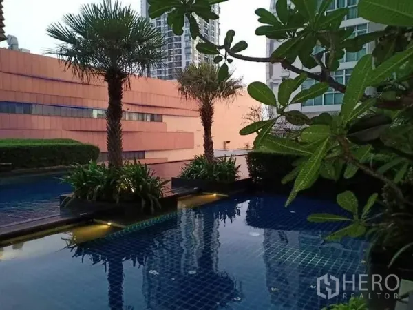 Condominium for rent in Khlong Luang, Pathum Thani - Condominium swimming pool with palm trees and greenery on a raised deck.