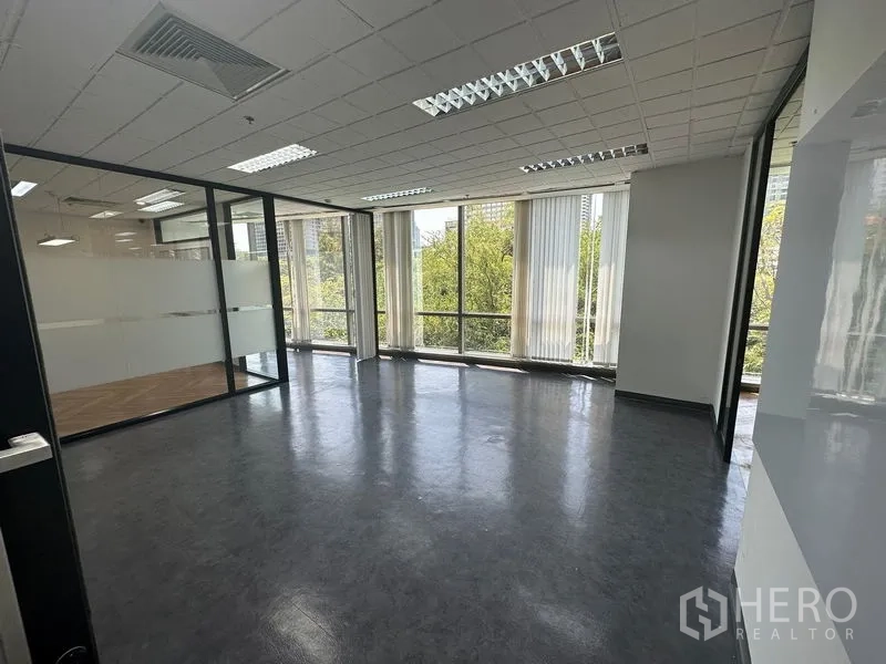 Office Space for rent - Bright room with glass walls and floor-to-ceiling windows overlooking greenery.