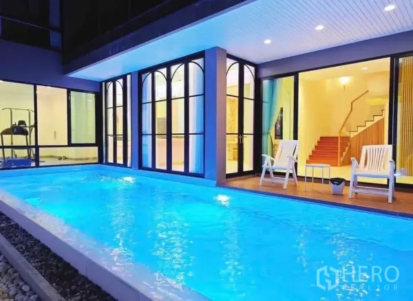 Detached House for rent in Phaya Thai, Bangkok - Illuminated private swimming pool beside glass-walled living area with deck chairs.