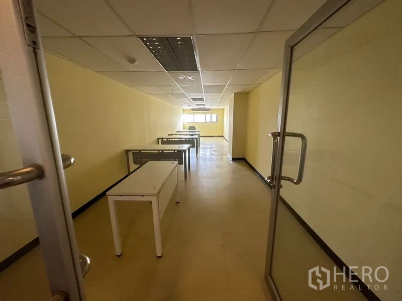 Office Space for rent in Watthana, Bangkok - Long office room with durable flooring, ceiling light panels, work tables and a rear window near Asok.