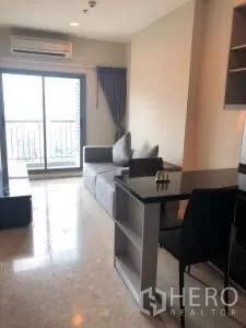 Condominium for rent or sale in Khlong Toei, Bangkok - Open-plan lounge with sliding glass doors to a balcony and a dining counter.