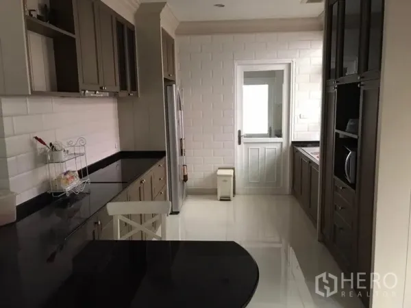 Detached House for rent in Bang Khen, Bangkok - Galley kitchen featuring white subway tiles, built-in cabinets and a door to utility area.