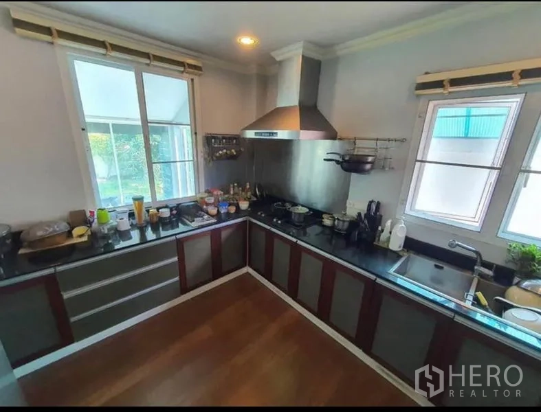 Detached House for sale in Sai Mai, Bangkok - L-shaped kitchen with stainless range hood, black countertops and twin windows.