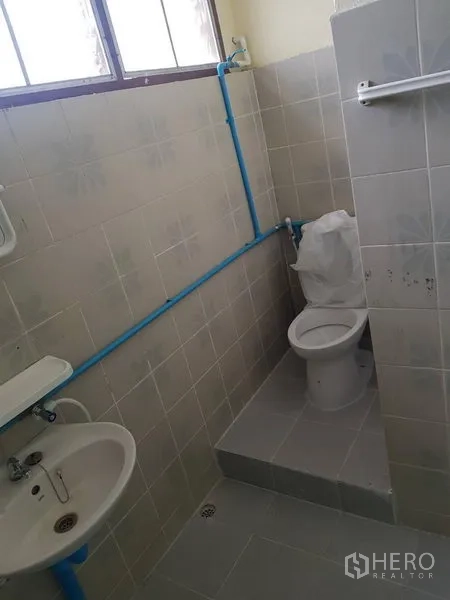 Retail Space for rent in Khlong Toei, Bangkok - Small bathroom with beige tiles, window, toilet, sink and exposed blue plumbing.