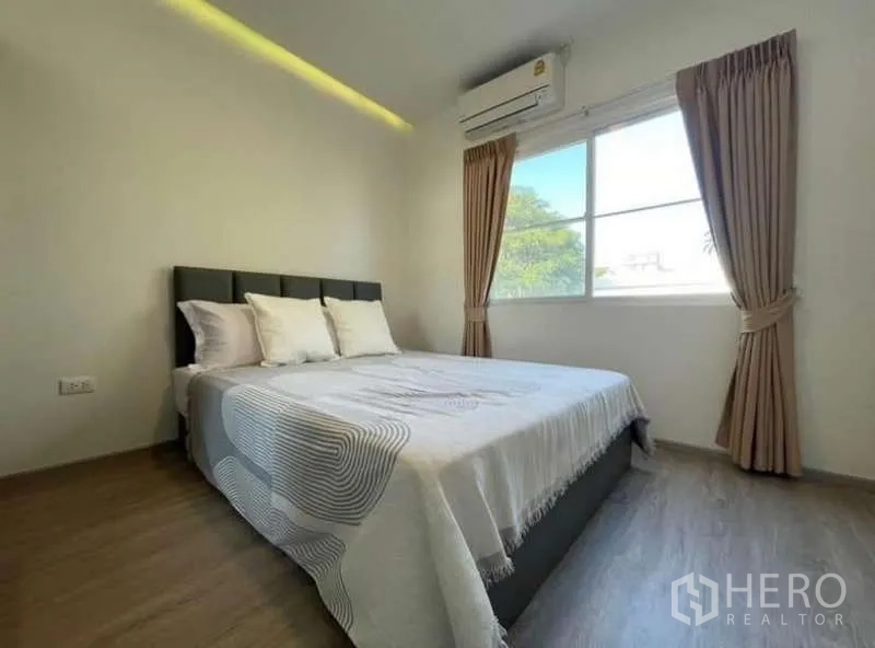 Townhouse for rent in Prawet, Bangkok - Bright bedroom with queen bed, window, curtains, and wood flooring