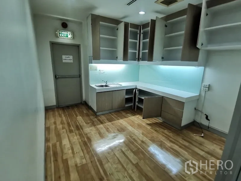 Office Space for rent in Bang Rak, Bangkok - Pantry kitchenette with upper cabinets, sink and under-cabinet lighting on wood floors.