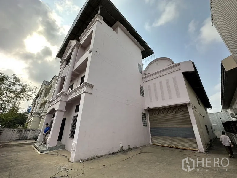 Factory for rent in Bang Bua Thong, Nonthaburi - Side elevation showing a wide concrete yard and roller-shutter loading door.