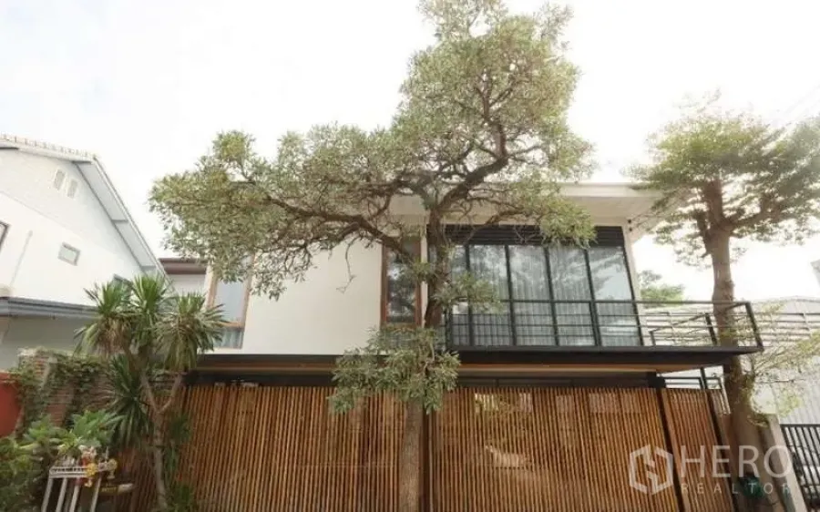 Detached House for rent in Lat Phrao, Bangkok - Contemporary two-storey house facade with balcony and vertical wooden screen.