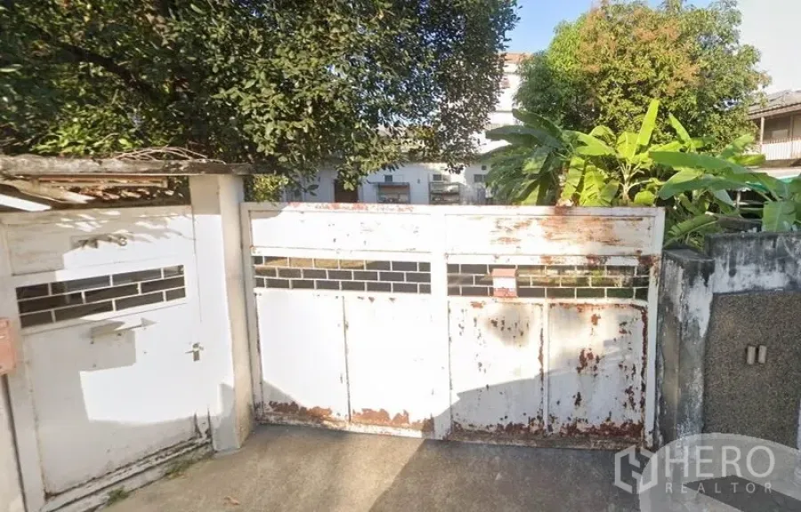 Home Office for rent in Chatuchak, Bangkok - White metal driveway gate with glass slots, weathered finish and lush trees at a home office in Chatuchak, Bangkok.