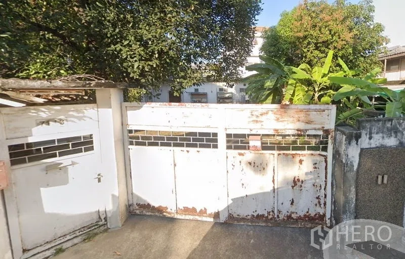 Home Office for rent in Chatuchak, Bangkok - White metal driveway gate with glass slots, weathered finish and lush trees at a home office in Chatuchak, Bangkok.