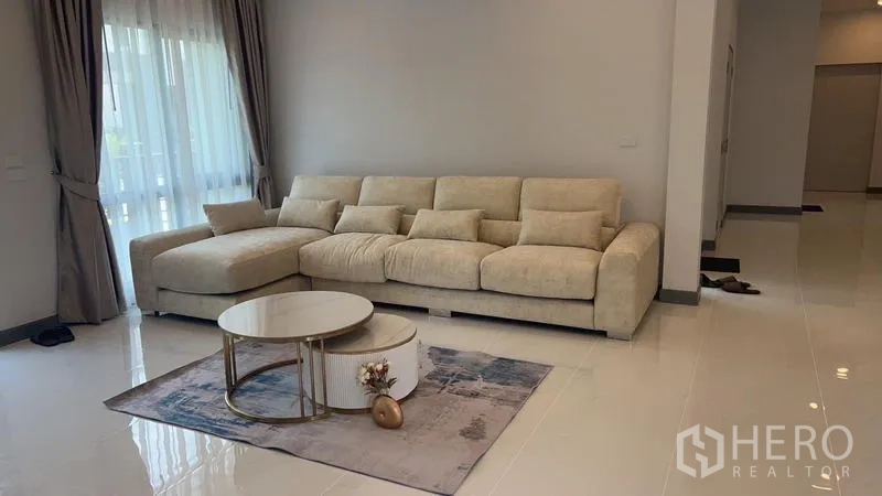 Detached House for rent - Living room with large beige sectional sofa, nesting coffee tables and full-height curtains.