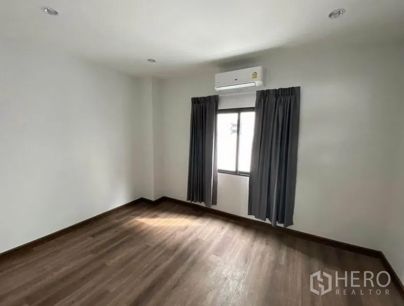 Townhouse for rent in Bang Na, Bangkok - Air-conditioned bedroom with wood flooring, white walls and a curtained window.