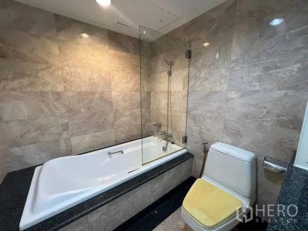 Condominium for rent or sale in Khlong Toei, Bangkok - Marble-tiled bathroom featuring a bathtub with handheld shower and glass screen.