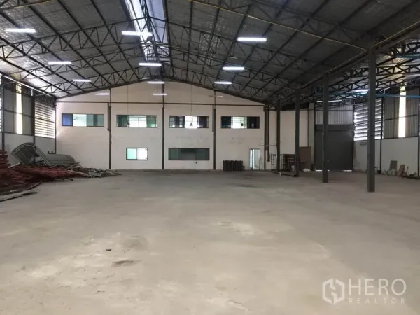 Warehouse for rent in Saphan Sung, Bangkok - Spacious warehouse interior with high steel truss roof, concrete floor, and windows to an attached office block.