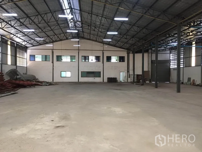 Warehouse for rent in Saphan Sung, Bangkok - Spacious warehouse interior with high steel truss roof, concrete floor, and windows to an attached office block.