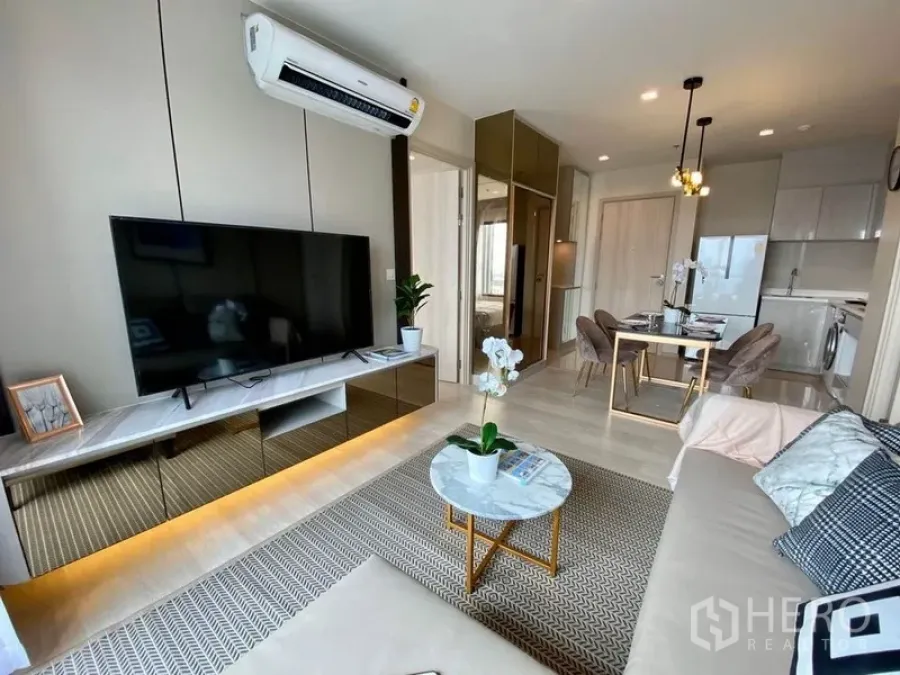 Condominium for rent in Pathum Wan, Bangkok - Open-plan lounge with TV, rug, and view toward the dining area and compact kitchen.