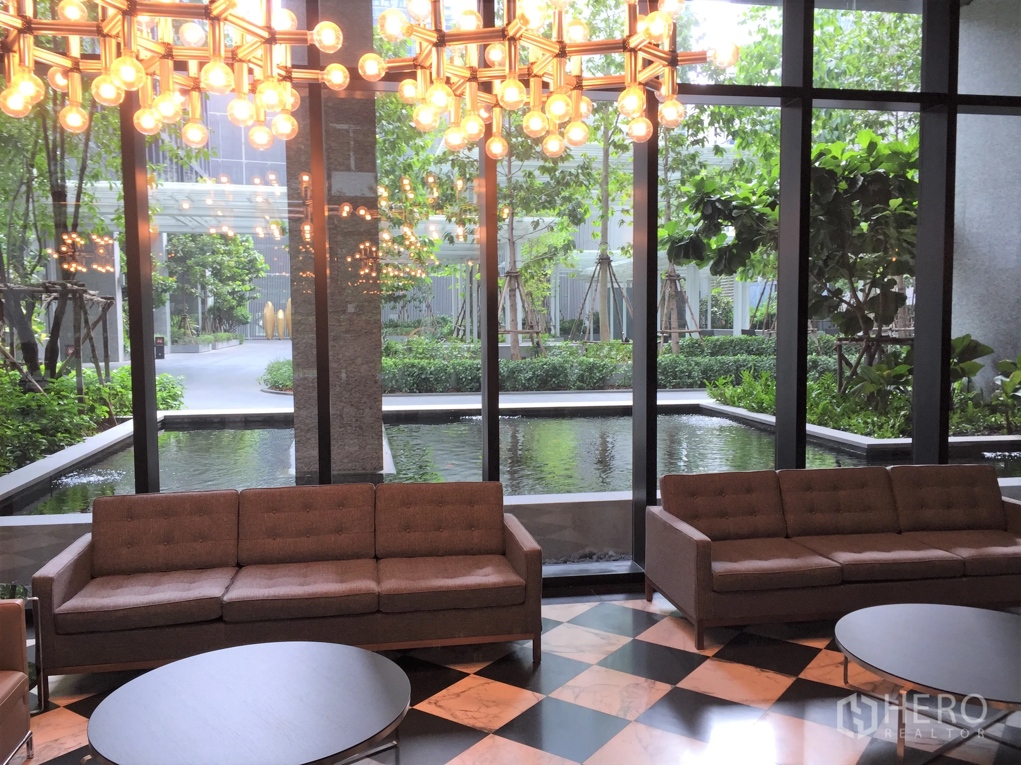 Condominium for rent in Pathum Wan, Bangkok - Condo lobby lounge with sofas, statement chandelier and garden view over a reflecting pool.