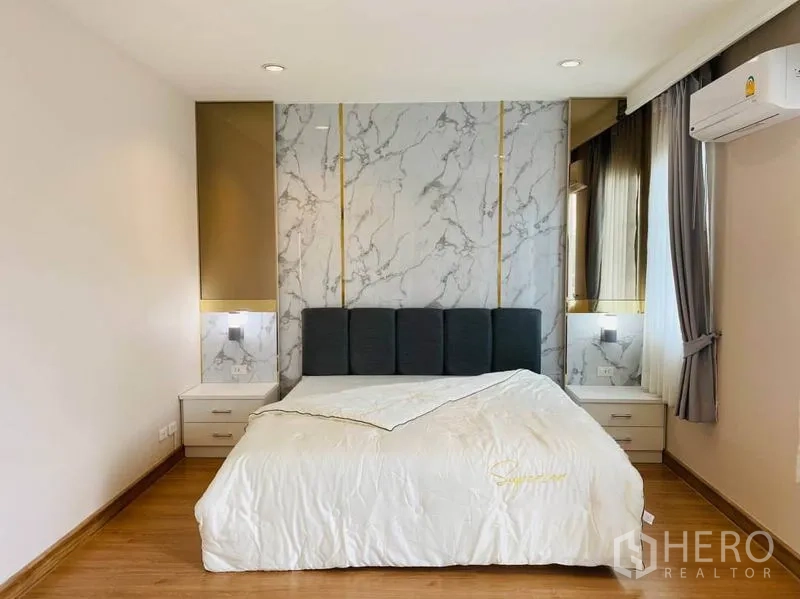 Detached House for rent in Suan Luang, Bangkok - Master bedroom with wood flooring, marble accent wall with gold trim and upholstered headboard.