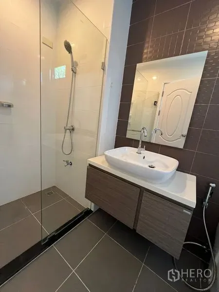 Townhouse for sale in Bang Kapi, Bangkok - Bathroom with glass shower enclosure and vessel sink against a brown accent wall.