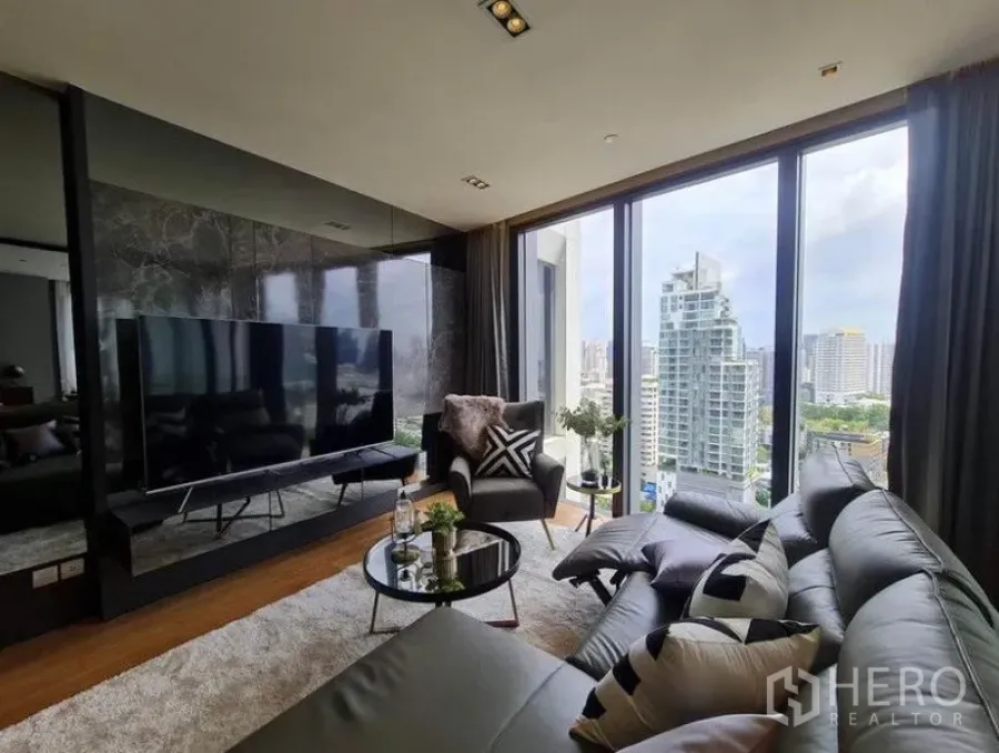 Condominium for rent in Khlong Toei, Bangkok - Modern living room with leather sofa, floor-to-ceiling windows and Bangkok skyline view.