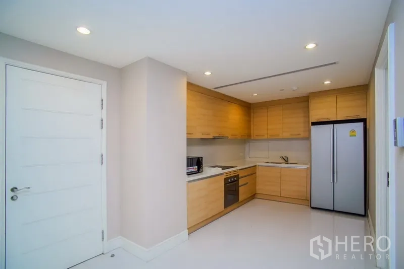Condominium for rent in Khlong Toei, Bangkok - Modern L-shaped kitchen with light wood cabinetry, built-in oven, cooktop, microwave and a double-door fridge.