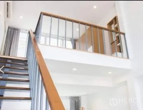 Townhouse for rent in Khlong Toei, Bangkok - Bright double-height interior with a wooden staircase and metal balustrade leading to a mezzanine.