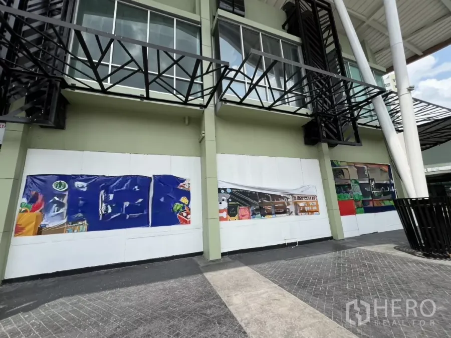 Retail Space for rent - Street-level shopfront with wide blank hoarding panels under metal awnings and upper glass windows.