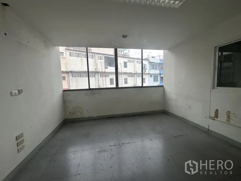 Office Space for rent in Khlong Toei, Bangkok - Compact office room with a large window overlooking neighboring buildings.