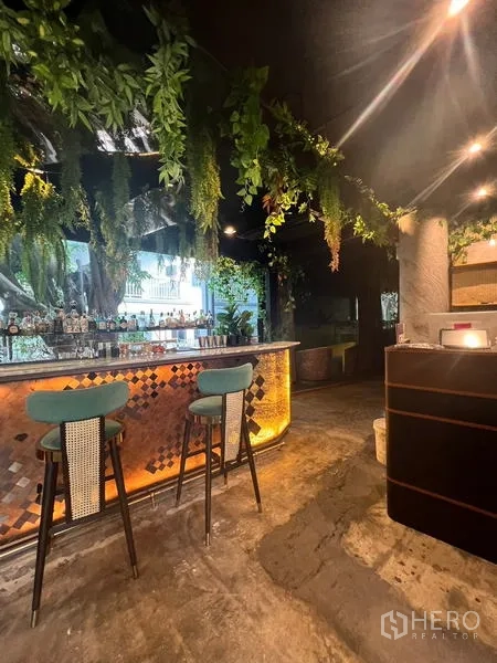 Retail Space for rent in Watthana, Bangkok - Side view of the illuminated bar and entrance area with ceiling plants and polished concrete floor.
