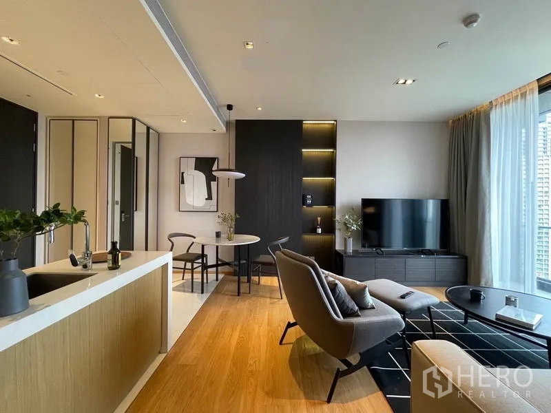 Condominium for rent in Khlong Toei, Bangkok - Modern lounge facing TV wall with round dining table, pendant light and compact kitchen island.