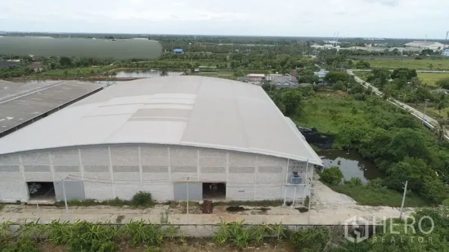 Factory for rent or sale in Krathum Baen, Samut Sakhon - Drone shot of a big single-span warehouse building with access road and ponds in green surroundings.