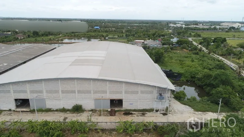 Factory for rent or sale in Krathum Baen, Samut Sakhon - Drone shot of a big single-span warehouse building with access road and ponds in green surroundings.