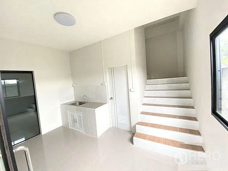 Factory for rent in Bang Bua Thong, Nonthaburi - Ground-floor kitchen area with stainless sink, glass door and stairs to upper level.