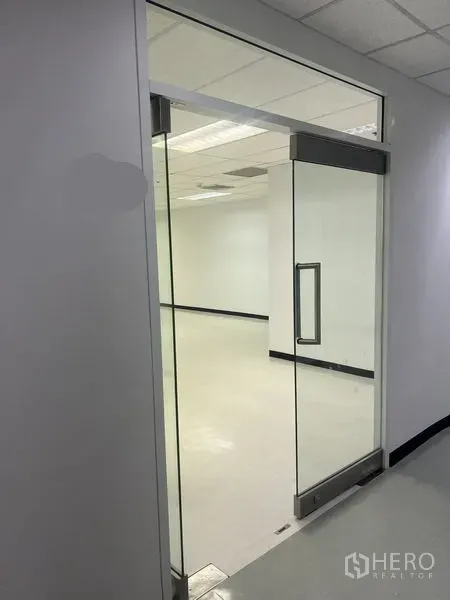 Office Space for rent in Watthana, Bangkok - Glass sliding entrance opens to a bright white office with drop ceiling lights.