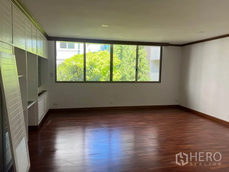 Townhouse for rent in Watthana, Bangkok - Large bedroom with dark wood flooring, broad window, and wall storage.