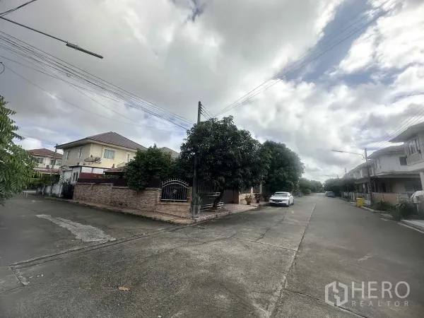 Detached House for sale in Pathum Thani - Quiet residential street inside a gated community with a corner house and wide roadway.