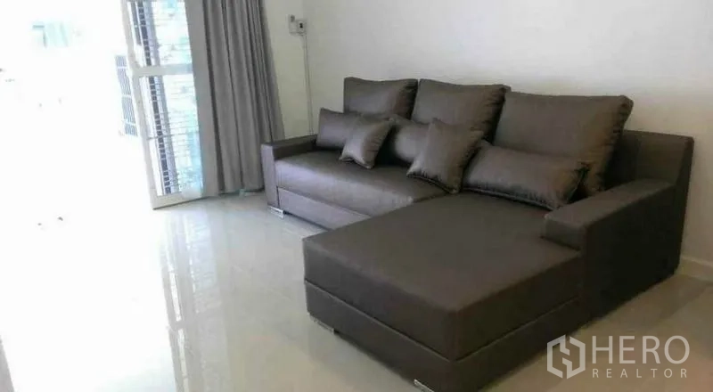 联排别墅 出租在Bang Phli, Samut Prakan - 采光良好的客厅，灰色L型沙发与亮面地砖。