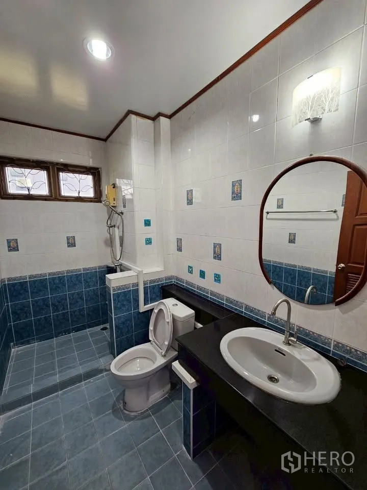 Home Office for rent in Wang Thonglang, Bangkok - Blue and white tiled bathroom with walk‑in shower, toilet and long vanity with round mirror.