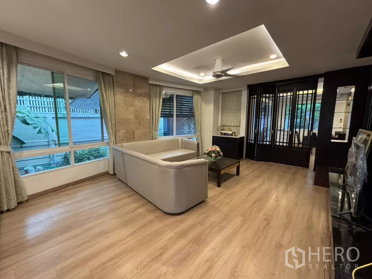 Detached House for rent in Bang Kapi, Bangkok - Open living room with L-shaped sofa, big windows, and recessed ceiling lights.