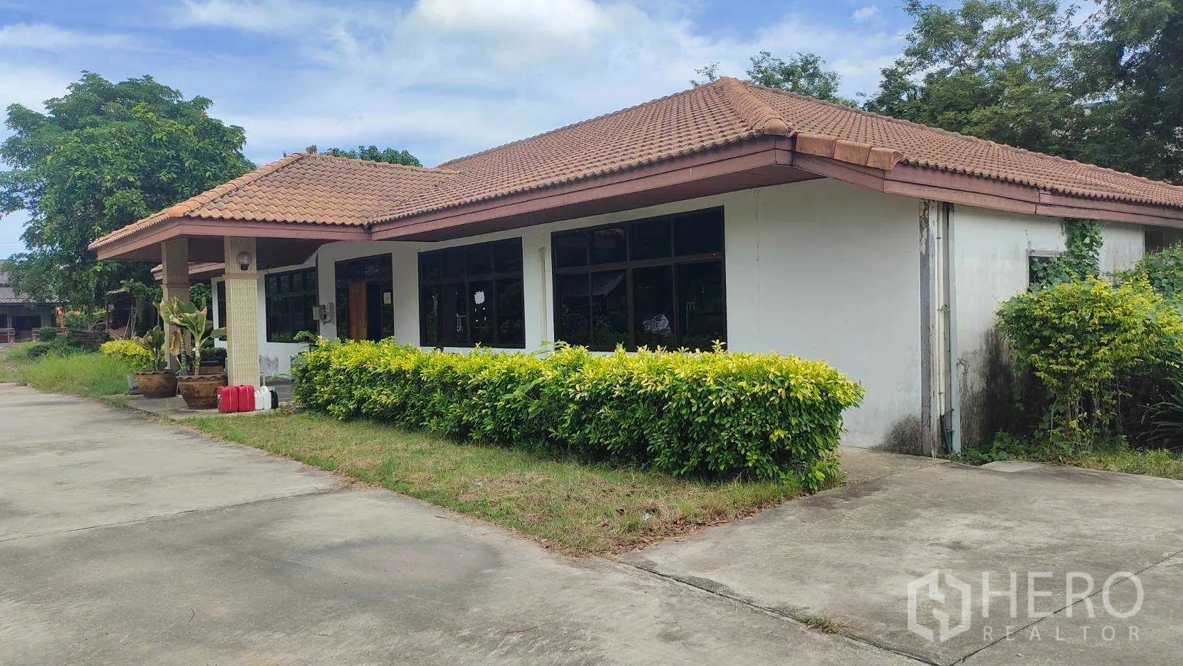 Factory for sale in Nikhom Phatthana, Rayong - Angled view of the office building with hedges and paved driveway.