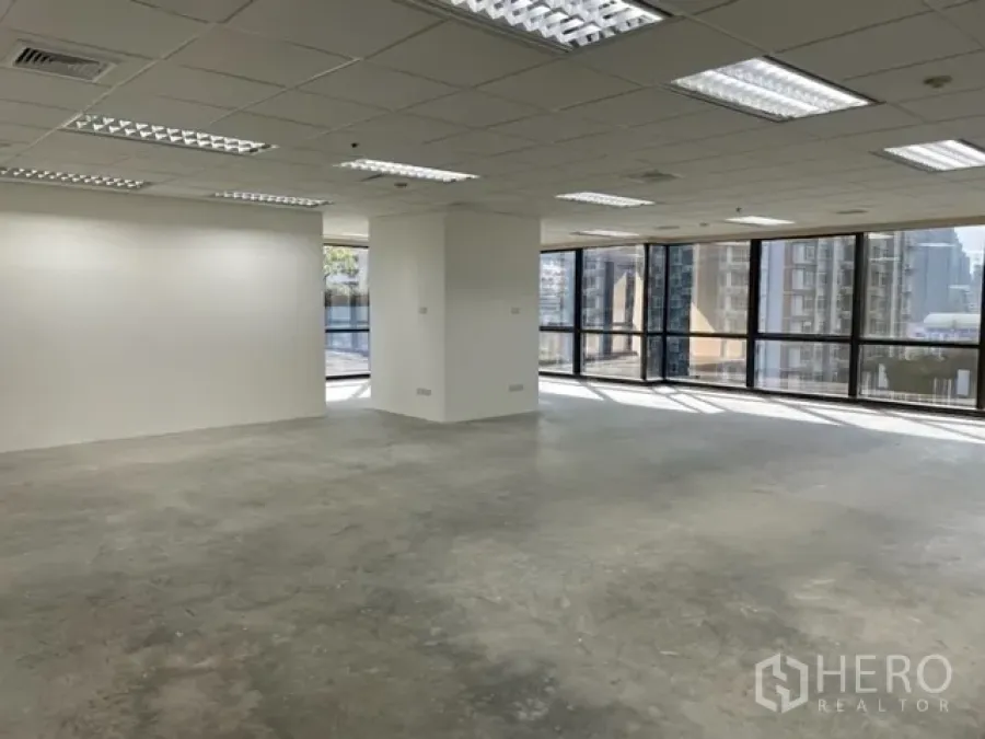 办公空间 出租在Ratchathewi, Bangkok - 明亮开放式办公室，网格吊顶与灯具、混凝土地面，转角落地窗俯瞰曼谷天际线（Ratchathewi）。