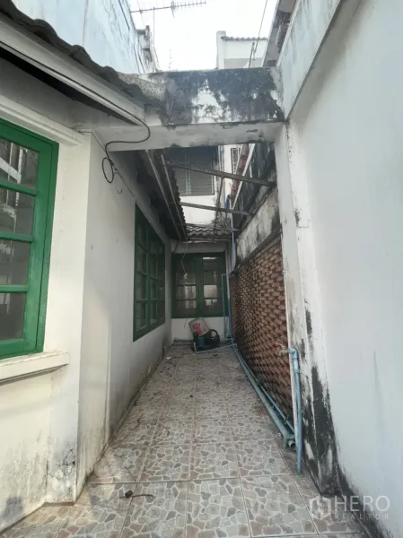联排别墅 出售在Watthana, Bangkok - 侧边狭长的瓷砖走道，绿色窗框与外露管线。