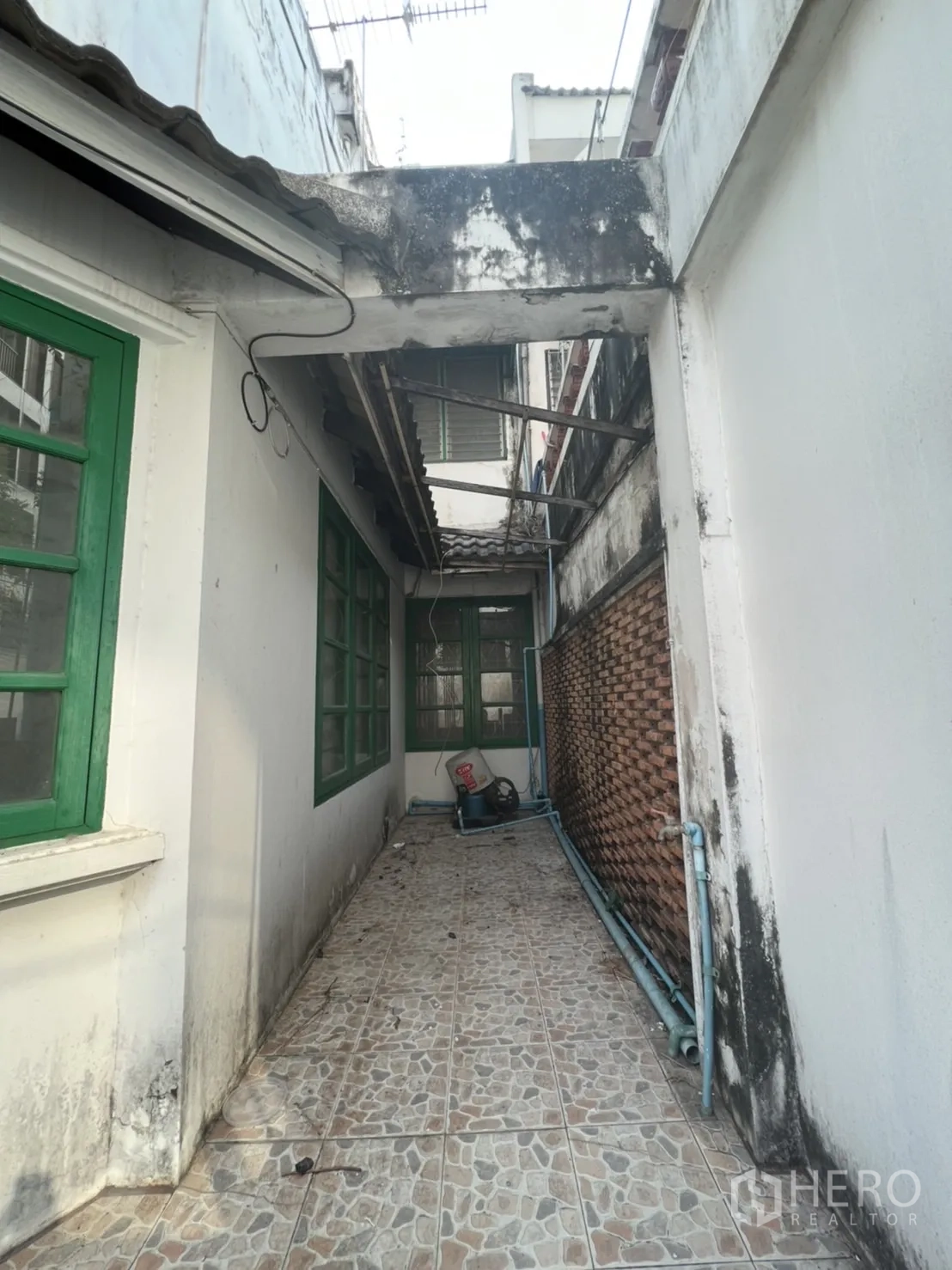 联排别墅 出售在Watthana, Bangkok - 侧边狭长的瓷砖走道，绿色窗框与外露管线。