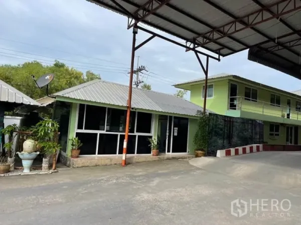 Warehouse for sale in Lam Luk Ka, Pathum Thani - On-site single- and two-story office buildings beneath a metal canopy with large windows and potted plants.