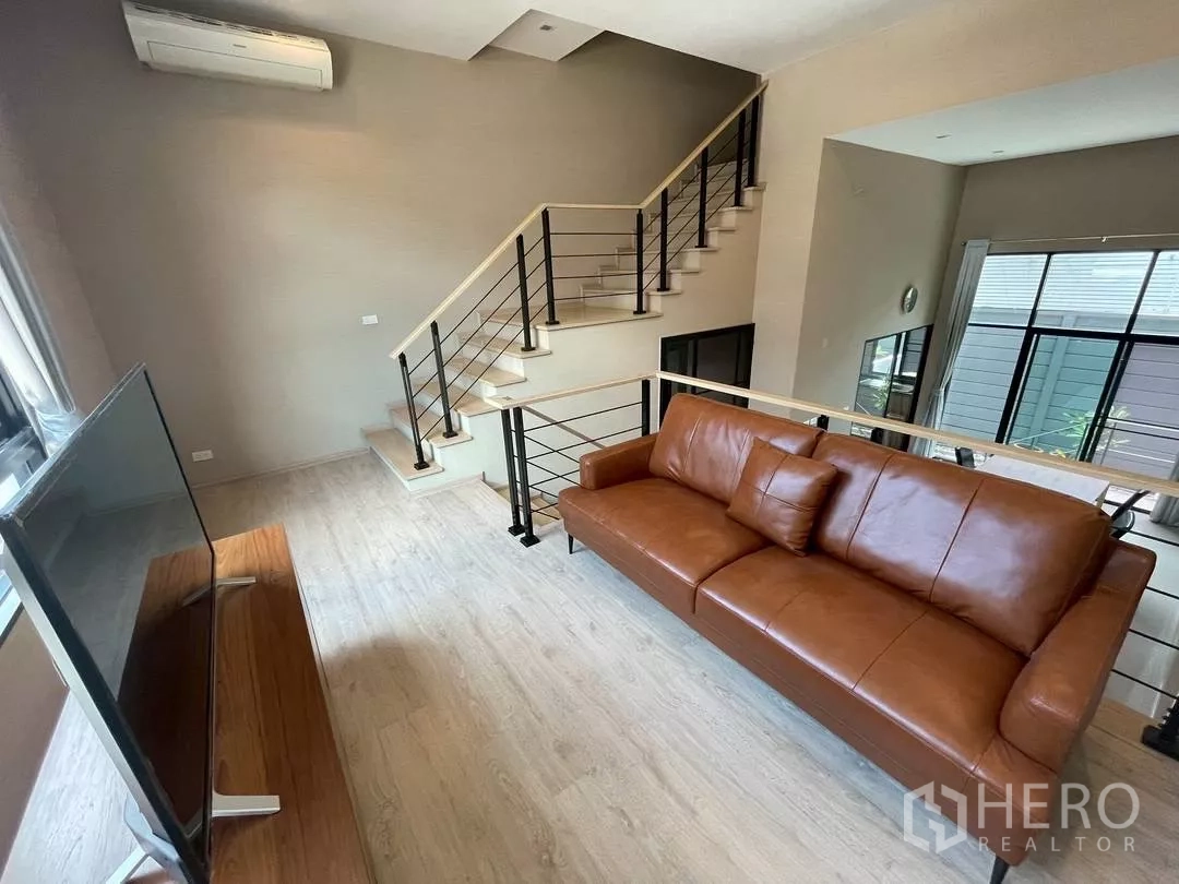 Townhouse for rent in Suan Luang, Bangkok - Open mezzanine living space with staircase, leather sofa and airy high ceilings.