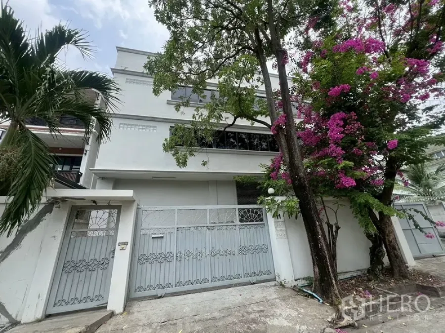 Warehouse for rent in Phra Khanong, Bangkok - Gated three-storey white warehouse facade with flowering trees in Phra Khanong