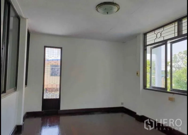 Detached House for rent in Lat Phrao, Bangkok - Upstairs bedroom with wood floors, windows and a narrow glass door to a balcony.