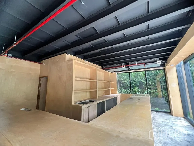 Retail Space for rent in Watthana, Bangkok - Retail space interior with plywood bar, open black ceiling and full-height windows facing greenery in Watthana, Bangkok.