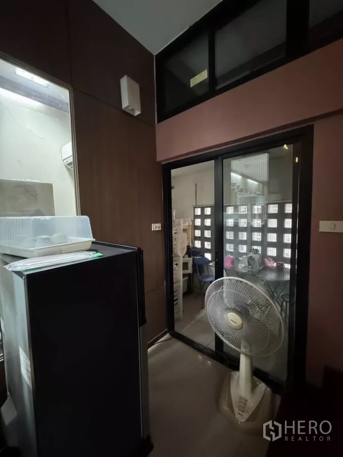 Shophouse for rent in Bang Rak, Bangkok - Compact utility nook with refrigerator, sliding glass door, and standing fan.