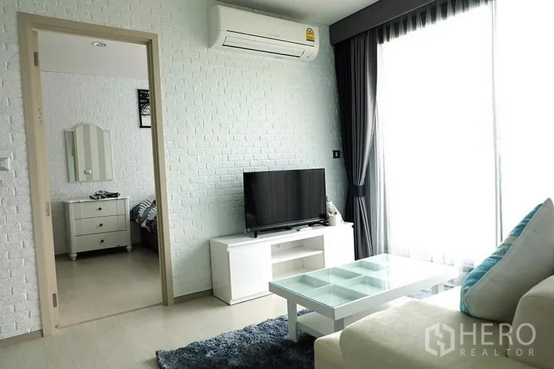Condominium for rent in Khlong Toei, Bangkok - Living area with TV console, air conditioner and sliding glass door to the balcony.